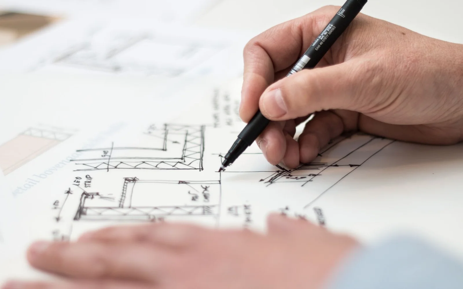 Hånd som tegner på plantegning - relevant for valg mellom ferdighus og arkitekttegnet hus